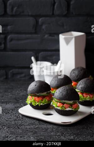 Hamburger noir avec tartare de saumon fumé, concombre, laitue et fromage à la crème, sélectif Banque D'Images