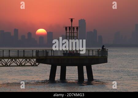 Koweït City / Koweït - 05/09/2019: L'homme a silhoueté la pêche sur la jetée avec vue sur la ville et coucher du soleil Banque D'Images