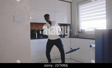 Joyeux homme noir beau à l'écoute de la musique et à l'utilisation du balai comme guitare. Fatiguant l'appartement. Photo de haute qualité Banque D'Images