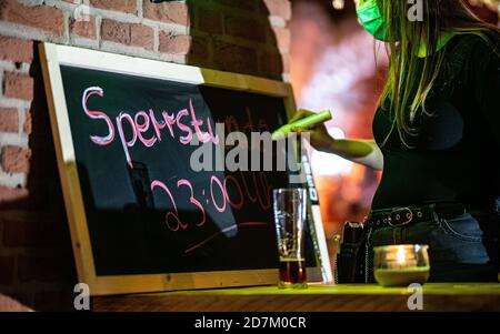 Warendorf, Allemagne. 23 octobre 2020. Une serveuse du bar n°1 à Warendorf, écrit: 'Temps de fermeture 23:00' sur un tableau de craie. En Rhénanie-du-Nord-Westphalie, un temps de fermeture obligatoire entre 23:00 et 6:00 a été introduit pour le commerce de la restauration dans toutes les communautés avec un grand nombre de nouvelles infections de corona. Le couvre-feu s'applique dans les municipalités de 50 nouvelles infections ou plus pour 100,000 habitants dans un délai de sept jours. Credit: Guido Kirchner/dpa/Alay Live News Banque D'Images