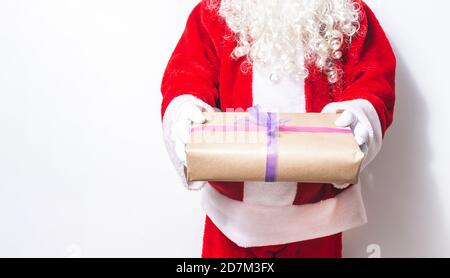 Le Père Noël dont le visage barbu est méconnaissable offrant un cadeau Avec ses deux mains à Noël sur fond blanc Banque D'Images