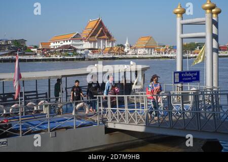 Les passagers débarquent d'un ferry traversant la rivière à l'embarcadère d'Atsadang (Yodpiman) près de la rivière Chao Phraya à Bangkok, en Thaïlande; b/g: (temple) Wat Kalayanamit Banque D'Images