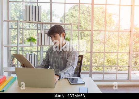 De jeunes hommes asiatiques s'assoient et travaillent à un bureau dans le bureau. Banque D'Images