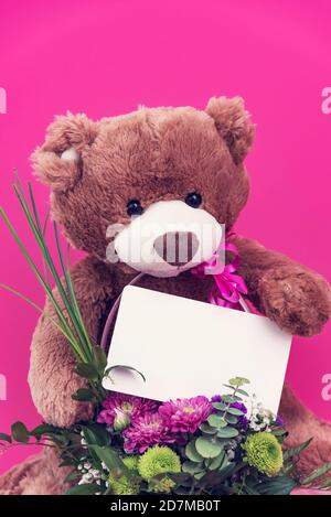 Ours en peluche contenant une carte vierge et un petit bouquet de couleur rose Banque D'Images