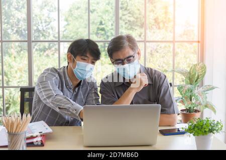 Un homme asiatique âgé avec un protège-bouche apprend à commercer en ligne via Internet avec un jeune homme qui enseigne et porte Matt. Banque D'Images