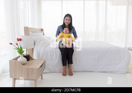 Une maman asiatique joue avec plaisir avec son bébé au lit. Banque D'Images