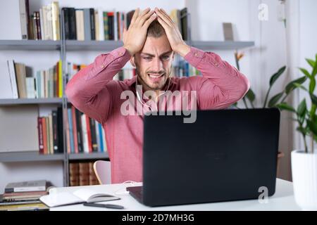 Jeune homme attrayant assis à la table au travail à la maison avec un pc portable inquiet et frustré Banque D'Images