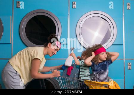 Mère ménage avec enfants portant des pyjamas avoir du plaisir et faire de la lessive à la laverie libre-service près des machines à laver. Les travaux ménagers ensemble Banque D'Images