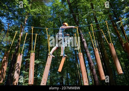 Un garçon muni d'un casque et d'une assurance passe par un parcours d'obstacles de haute altitude. Entraînement Banque D'Images