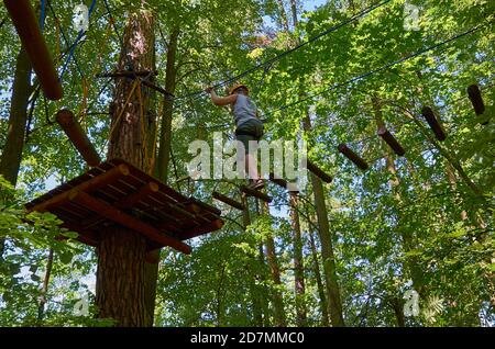 Un garçon muni d'un casque et d'une assurance passe par un parcours d'obstacles de haute altitude. Entraînement Banque D'Images