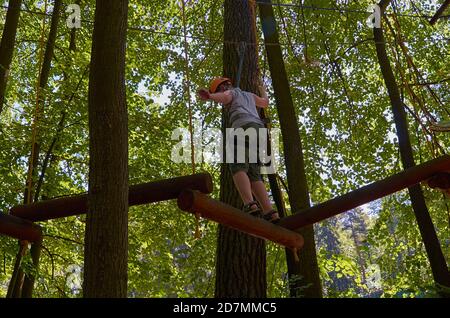 Un garçon muni d'un casque et d'une assurance passe par un parcours d'obstacles de haute altitude. Entraînement Banque D'Images