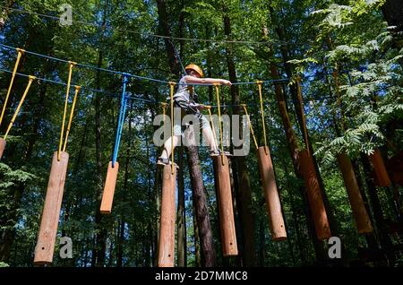 Un garçon muni d'un casque et d'une assurance passe par un parcours d'obstacles de haute altitude. Entraînement Banque D'Images