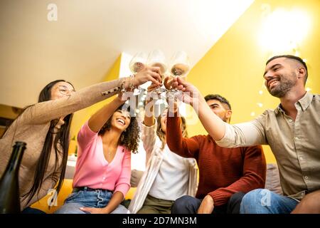 Vue de dessous d'un groupe multi-ethnique de jeunes amis à maison assise sur le canapé avec des verres à vin blanc - les gens heureux multiraciaux ayant le plaisir d Banque D'Images
