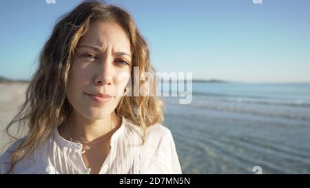Gros plan sur une jeune femme blonde caucasienne mignonne la caméra au coucher du soleil ou à l'aube dans la mer avec Une chemise blanche élégante, véritable co Banque D'Images