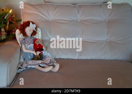 Poupée de chiffon d'ange de Noël tenant l'ours en peluche de santa, sur un canapé en velours, à côté de l'arbre de Noël décoré. Copier l'espace pour le texte. Décoration de Noël Banque D'Images