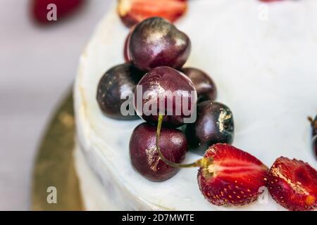 Cerises et fraises à l'or comestible sur le cheesecake à la noix de coco. Banque D'Images