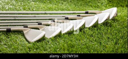 Clubs de golf situés sur une pelouse verte, reflets de la lumière du soleil, vue rapprochée. Concept d'équipement et de sport de golf, bannière. Banque D'Images
