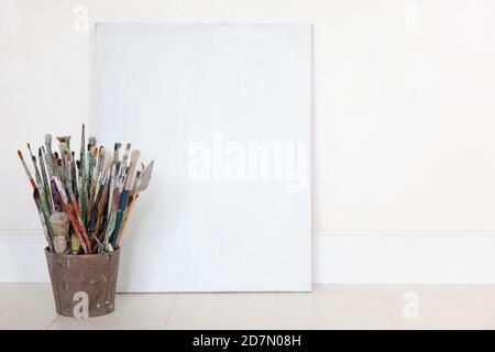 Toile encadrée debout avec pile de pinceaux à huile et couteau à peindre dans un seau marron. Banque D'Images