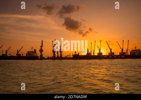 Kandla,20 août, 2019 : Silhouette de grues et de navires contre le coucher de soleil d'or avec réflexion dans la mer d'Arabie à Deendayal Port Trust, Kandla,Kutch, Banque D'Images