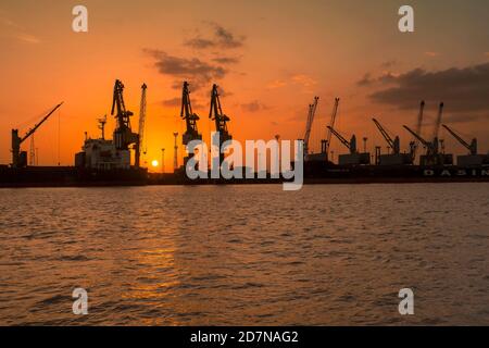 Kandla,20 août, 2019 : Silhouette de grues et de navires contre le coucher de soleil d'or avec réflexion dans la mer d'Arabie à Deendayal Port Trust, Kandla,Kutch, Banque D'Images