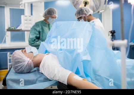 Jeune homme patient dans un masque de protection et des vêtements de tête couchés tableau des opérations Banque D'Images