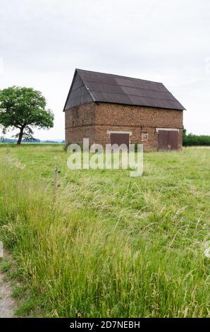 Grange abandonnée faite de briques rouges avec des portes en bois dans un champ agricole d'herbe la campagne rurale, Allemagne, Europe occidentale Banque D'Images