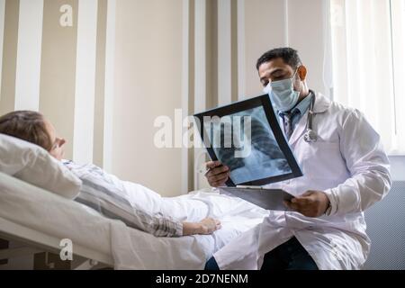 Jeune radiologue en blancoat et masque regardant le poumon du patient image radiologique Banque D'Images