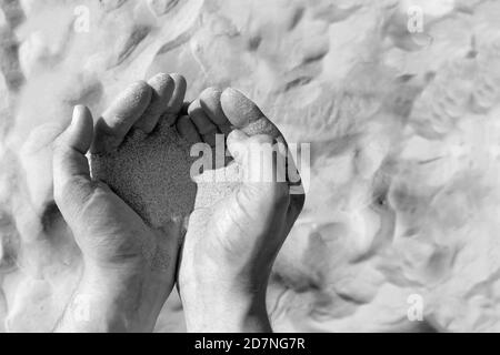 Sable dans les mains mâles sur fond de sable / désert. Photo en noir et blanc Banque D'Images