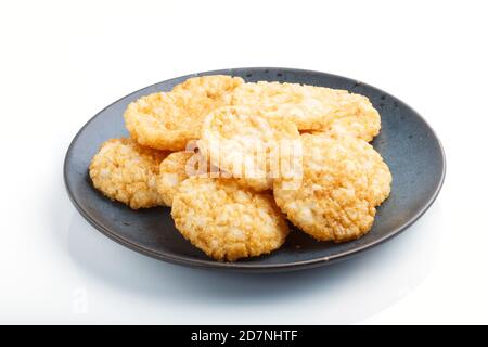 Biscuits japonais traditionnels aux croustilles de riz avec sauce au miel et au soja sur une plaque en céramique bleue isolée sur fond blanc. Vue latérale, gros plan, Banque D'Images