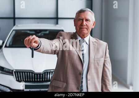 Homme joyeux et vieux en tenue habillée se tient devant voiture blanche moderne Banque D'Images