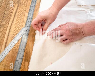 la main du concepteur fixe les dispositions de coupe de papier de la robe à calico tissu avec épingles sur une table en bois à la maison Banque D'Images
