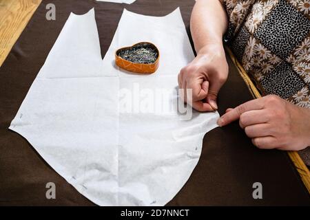 l'application sur mesure fixe la disposition en papier de la robe au tissu brun par des épingles sur une table en bois à la maison Banque D'Images