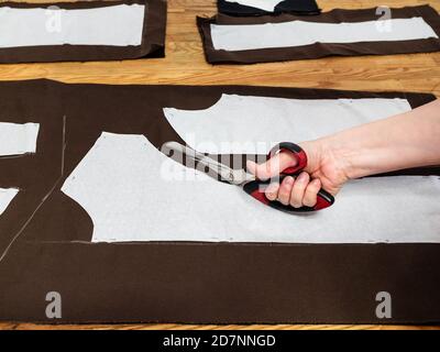 la main coupe le tissu brun par des ciseaux selon les dispositions de motif de robe sur table en bois à la maison Banque D'Images