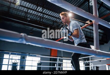 Jeune homme en chemise blanche et gants de protection faisant des exercices en anneau de boxe Banque D'Images
