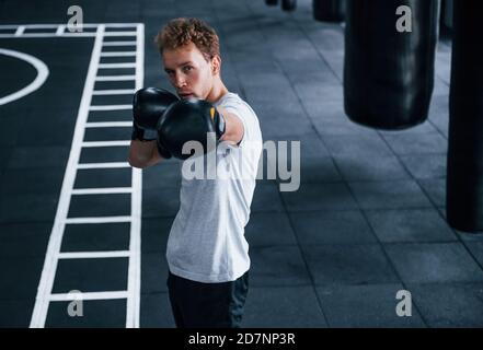 Jeune homme en chemise blanche et gants de protection de boxe faisant exercices dans la salle de gym Banque D'Images