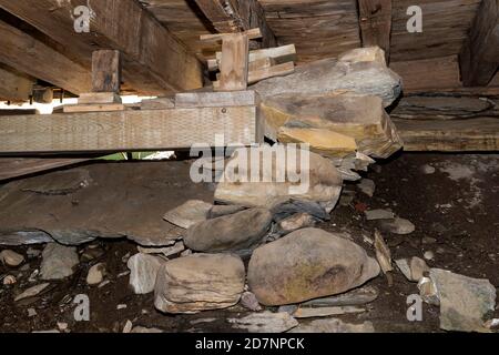Un tas de rochers, des blocs de bois et une poutre en bois maintiennent un plancher dans un sous-sol inachevé. Le sol est sale et rocailleux. La lumière extérieure est visible à travers Banque D'Images