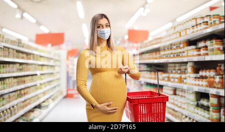 Femme enceinte avec un panier portant un visage protecteur masque et pose dans un supermarché Banque D'Images