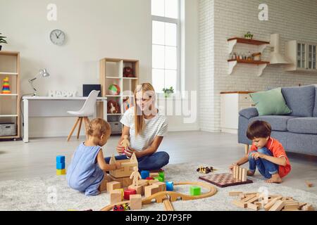 Mère heureuse et ses deux enfants à la maison, jouant avec beaucoup de blocs de bois, la construction de la grande ville de jouets Banque D'Images