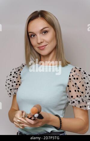 Concept de maquillage. Femme souriante utilisant la brosse cosmétique application de la poudre de visage pose sur fond gris dans Studio Banque D'Images