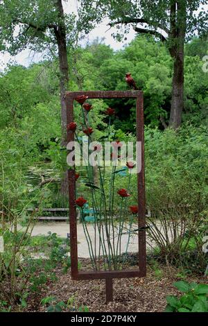 Une sculpture en métal 3D de roses à longue tige encadrées dans un rectangle en métal avec un cardinal en métal perché sur le cadre dans un parc boisé à Janesville, Banque D'Images