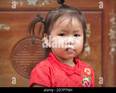 Mignonne petite fille chinoise thaïlandaise avec des queues de porc drôles porte une robe traditionnelle chinoise en soie rouge et or (cheongsam) pendant le nouvel an chinois. Banque D'Images