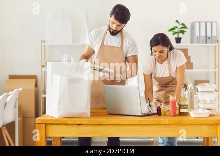 Les employés d'un restaurant d'aliments sains enregistrent les données et emballez les contenants d'aliments pour livraison. Banque D'Images