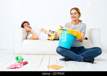 Le mari repose sur le canapé pendant que sa femme nettoie vers le haut de la décoration intérieure Banque D'Images