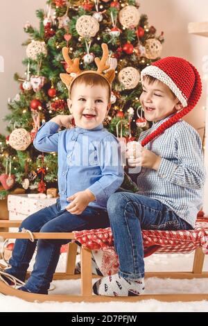 Adorables et heureux petits frères en traîneau s'amuser Avant de l'arbre de Noël et de la cheminée - Joyeux Noël Banque D'Images