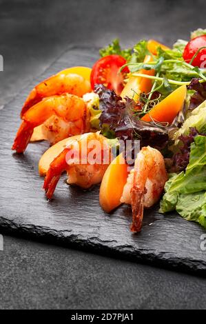 Salade fraîche avec crevettes sur une assiette noire. Banque D'Images
