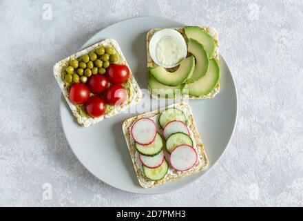 Des sandwiches faits maison avec des tomates cerises, du radis, du concombre, de l'avocat et du pois vert sur une assiette grise reposent sur un fond clair. Tranches de légumes Banque D'Images