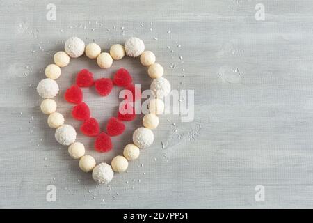 Saint Valentin. Un coeur de bonbons ronds blancs et de marmelade rouge sous forme de coeurs est disposé sur un fond blanc en bois. Composition de la pose à plat Banque D'Images