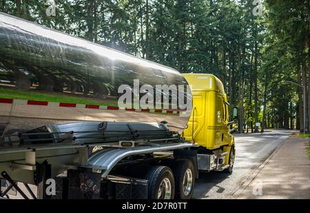 Tracteur semi-remorque diesel industriel Big RIG jaune brillant avec compartiment de cabine étendu transportant le carburant dans un réservoir semi en acier inoxydable remorque en marche Banque D'Images