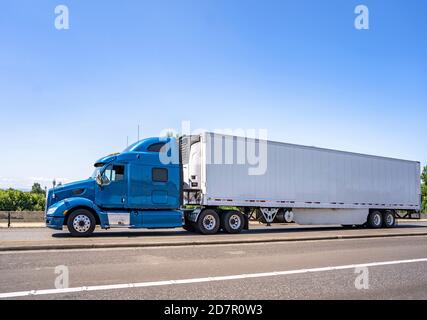 Capot de qualité industrielle de gros engin bleu, long transporteur diesel semi chariot avec cabine à toit surélevé et réfrigérateur semi-remorque en marche avec chargement commercial sur t Banque D'Images