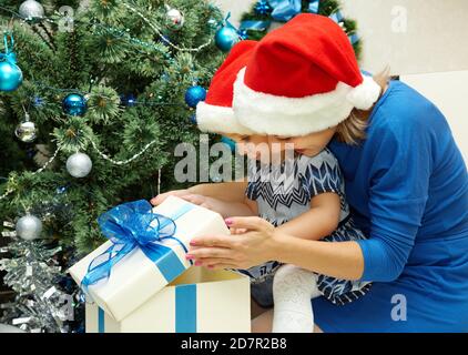 La mère donne un cadeau enfant dans une boîte cadeau. Jeune famille célébrant Noël à la maison. Nouvel an et Noël personnes Banque D'Images